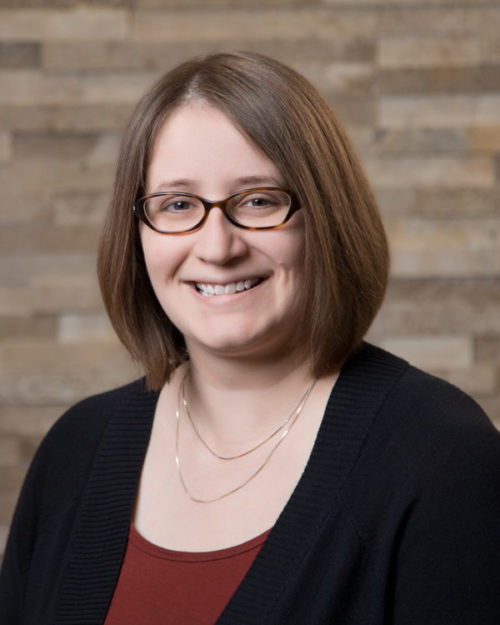 Portrait of Jennifer, a smiling pale-skinned, bespectacled woman.