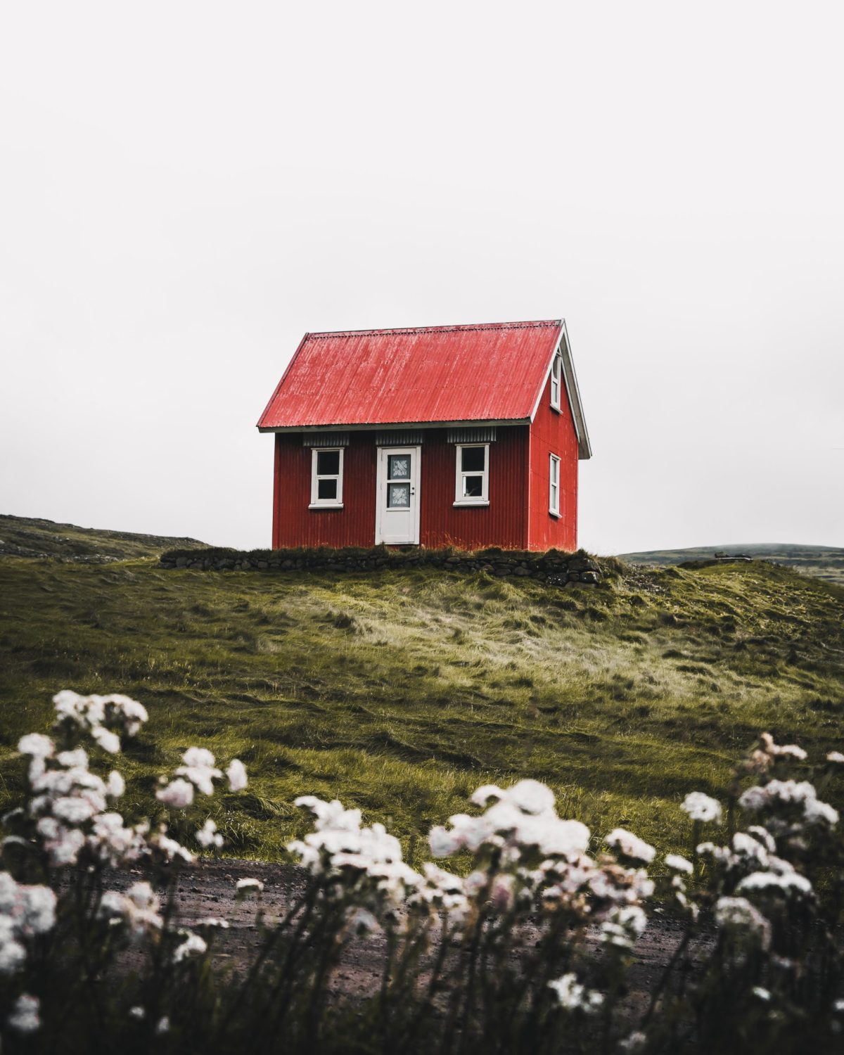 A small red house sits atop a grassy hill.